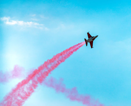 Silhouette sport aircraft with propellers, performing tricks with a red smokescreen against the blue...