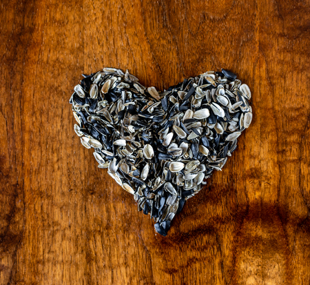 Heart made of black sunflower seed husk isolated on a wooden table. Top viewの写真素材