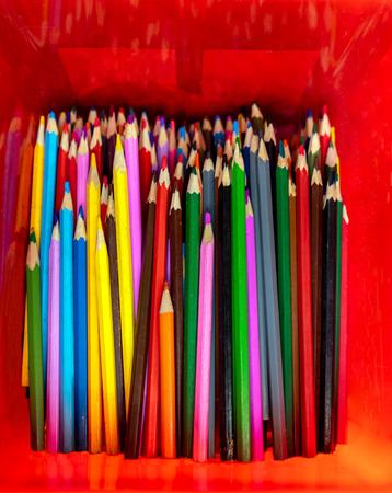 Lot of wooden colored pencils, sharpened with a knife and neatly stacked in a red box close-upの写真素材