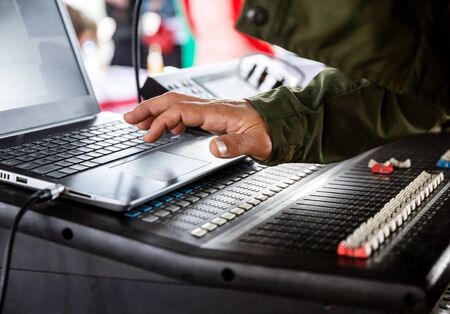 DJ's hand over the laptop and mixing console controlling the sound settingsの写真素材