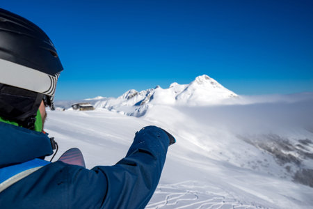 Snowboarder freerider points to the snow field to descend from the top of Caucasus mountains in...