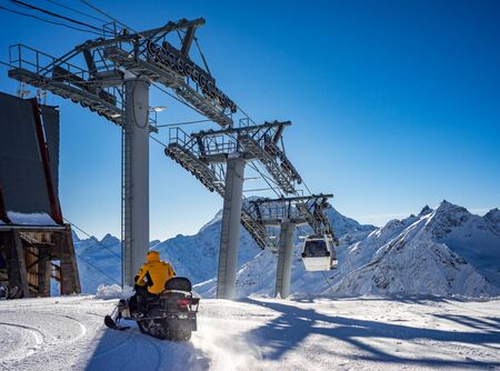 Snowmobile with a driver in motion. Cableway in movement on rise and descent on background beautiful landscape of snowy high mountains Caucasus Elbrusの写真素材