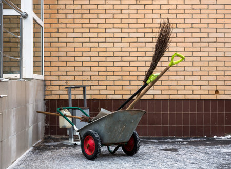 Tools of janitor in the cart, brooms and shovels near wall of brick house 