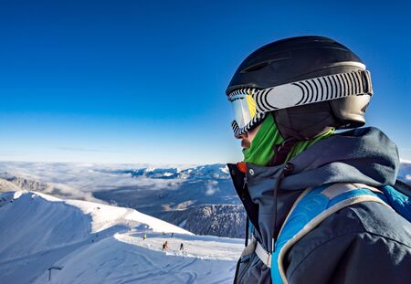 Portrait of young snowboarder in helmet and sunglass mask at the ski resort Rosa Khutor on background of the mountain range and the blue skyの写真素材
