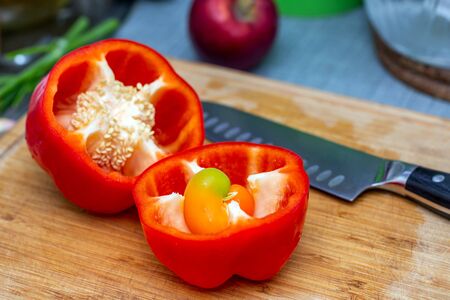 Bell red pepper cut into two parts with a large kitchen knife closeup on a bamboo board. Inside the pepper, like a sprout germの写真素材