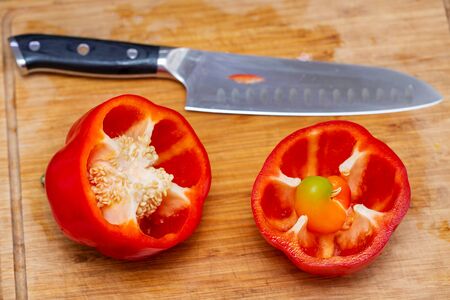 Bell red pepper cut into two parts with a large kitchen knife closeup on a bamboo board. Inside the pepper, like a sprout germの写真素材