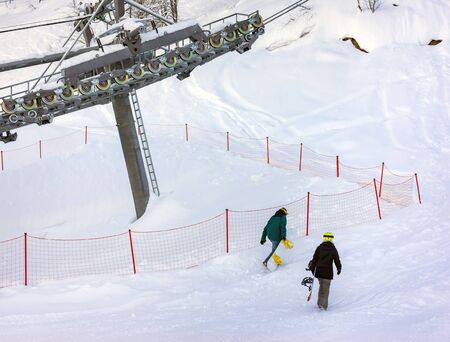 Snowboarders freeriders climb up the mountain under the cable car on the ski resortの写真素材