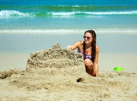 Happy young woman building a sandcastle on the beachの写真素材