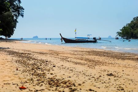 Fishing motor boat anchored near the shore at low tide. People swimming in the seaの写真素材