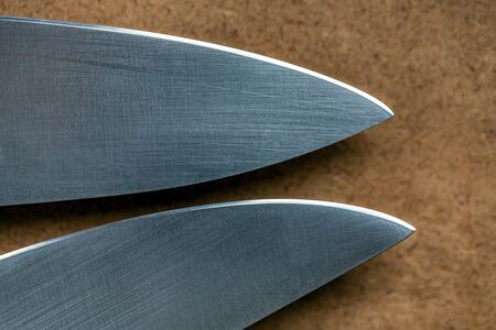 Cutting edge of two kitchen knives closeup. Tips of knives on background of wooden surfaceの写真素材