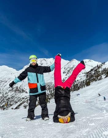 Happy funny couple on the background of snowy mountains. Standing upside down and showing OK signの写真素材