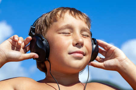 Boy listens to music on headphones on background of blue skyの写真素材