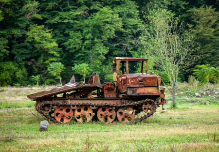 Old rusty all-terrain vehicle on tracks in an open field near the forestの写真素材