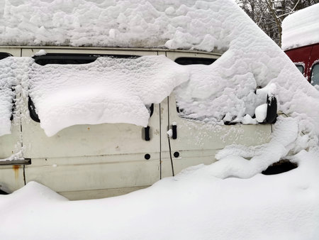 Cars covered with snow in the parking in the yard near a houseの写真素材