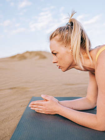 Young blonde woman doing workout outdoors on the sand. Modern healthy lifestyle.の写真素材