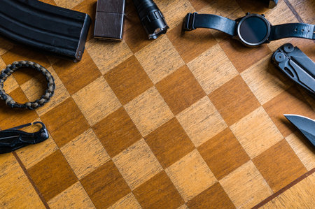 Military EDC concept on chess board background. Survival knife, M4 mag, smartwatch, tourniquet,...