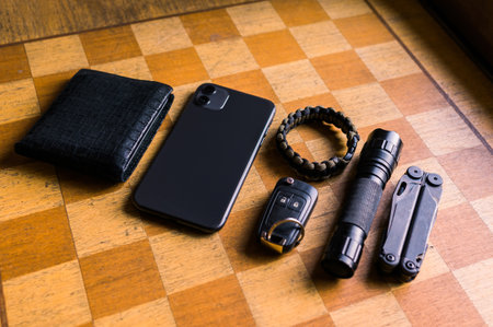 EDC setup. Concept on the wooden chess board. Everyday carry for a man. Knife, Multitool, Flashlight, Car key, Paracord bracelet, Wallet, Lighter, Smartphone...の写真素材