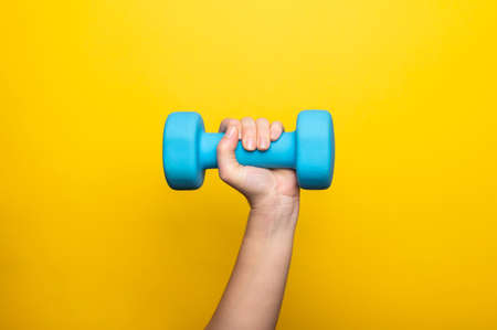 Woman's hand holding blue dumbbell isolated on pink background. Home workout, fitness, and activity. Sport and healthy lifestyle concept with copy space.の写真素材
