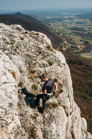 Young man rappelling down a rocky cliff, he is attached on rope with a figure eight and carabiner....