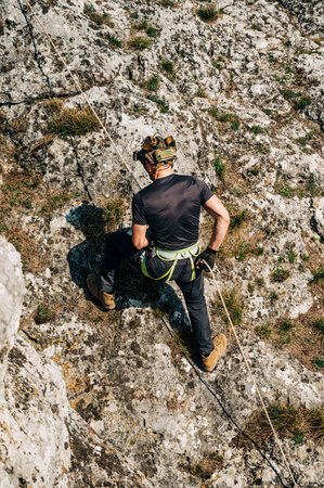 Young man rappelling down a rocky cliff, he is attached on rope with a figure eight and carabiner....