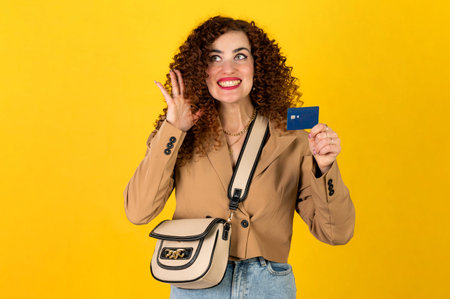 Curly girl in the trendy outfit of jeans and jacket posing with a shopping bag and credit card on...