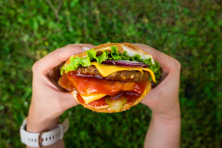 Hands holding a double cheeseburger. Hamburger food concept. Meat, salat, chesse and bread.