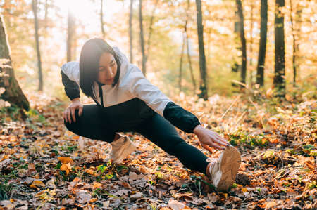 Portrait of young girl stretching during her exercise in the forest during the fall. Fitness outdoor concept.の写真素材