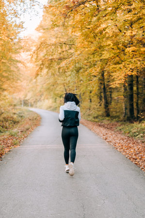 Girl jogging thru the forest in the fall season. Fitness outdoors concept.