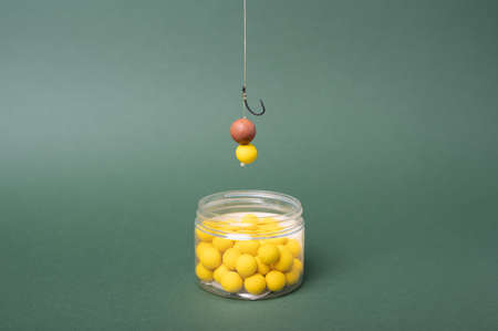 Carp fishing tackle concept, sharp fishing hook with boilie for carp fish. Yellow boilie on green backdrop.の写真素材