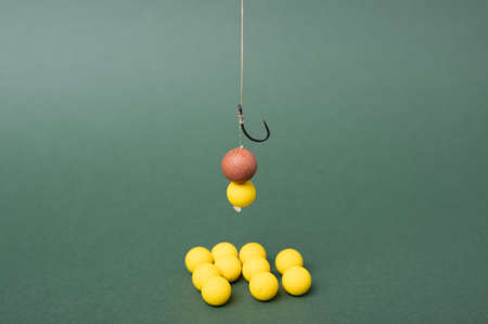 Carp fishing tackle concept, sharp fishing hook with boilie for carp fish. Yellow boilie on green backdrop.の写真素材