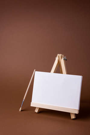 White canvas on a small wooden easel stand minimal concept on the brown backdrop. Empty blank mock up frame for design with copy space.の写真素材