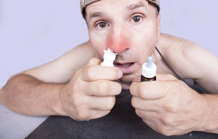 Sick man taking his nasal spray while holding nasal dropsの写真素材