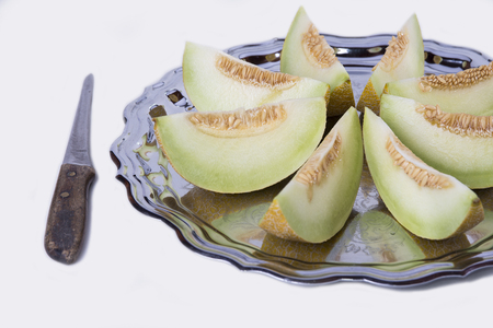 Slices of fresh yellow melon or cantaloupe  on the old tray with knifeの写真素材