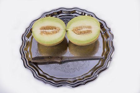 Yellow melon or cantaloupe on the old tray on the white background with knife cut in halfの写真素材