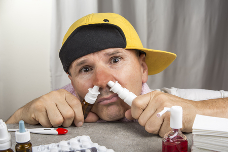 Cold concept. Sick man with the flu taking nasal spray.の写真素材