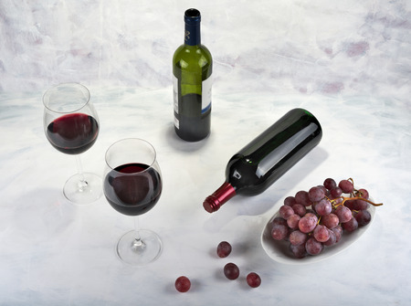 Two glasses of red wine with bottle and grapesの写真素材