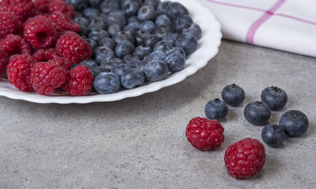Raspberries and blueberries on the plate and kitchen top.