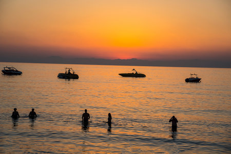 Sunset at the beach with boats and silhouette of swimming people.の写真素材