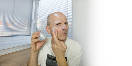 Senior man is putting a moisture cream on the faceの写真素材