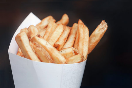 French fries in paper bundle. Dark background. Place for text and copyspace