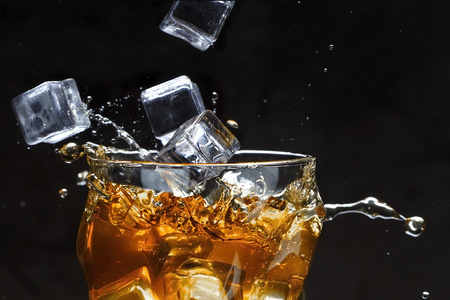 Ice cubes pour into a glass with alcohol. Splashes, dark background. Copy space for text.の写真素材