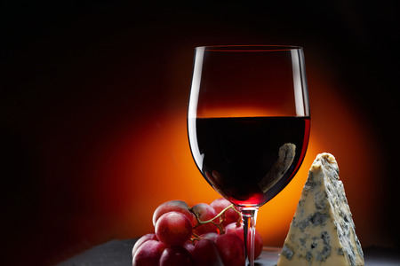 Glass of wine with grapes and a piece of cheese with mold. Orange background.の写真素材