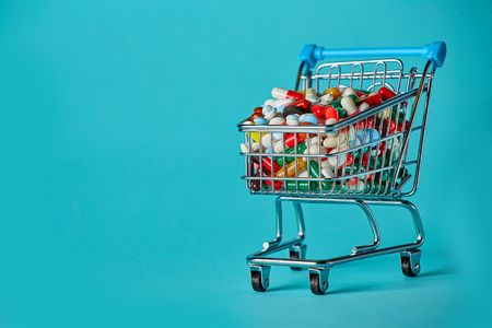 Shopping cart filled with pills. Blue background. Concept: full set of medicines in the store. Copy space for textの写真素材