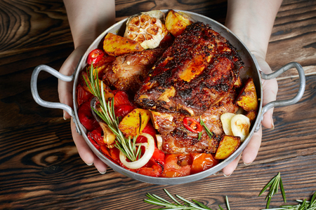 Hands holding fried ribs in a pan with rosemary, potatoes rustic, onion, sauce . Ribs are strung on a meat fork. Dark background. Place for text, copyspaceの写真素材