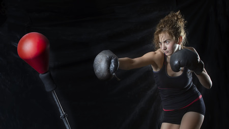 Beautiful Female Punching A Boxing bag With Boxing Gloves at the gym. concept about sport, fitness. Kickboxing and fight sport concept. Dark background. Space for text, copy space.の写真素材