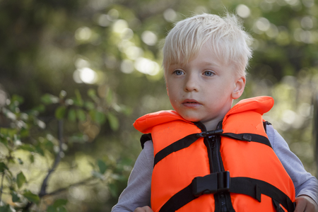 The boy is blond in a red life jacket.の写真素材