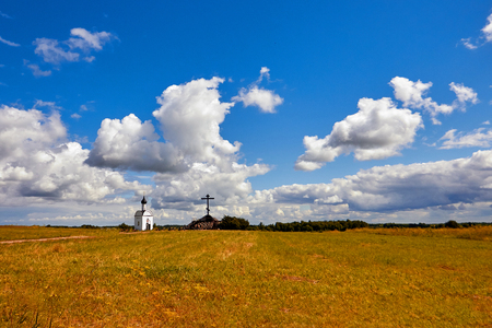 Yellow field with cross and Church under blue sky with clouds.の写真素材