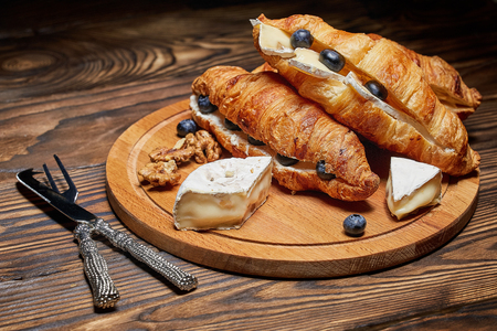 Croissants with cheese, nuts and blueberries, on a wooden Board with a knife and a fork for cheese. Concept: a beautiful presentation of the food with Cutlery.の写真素材