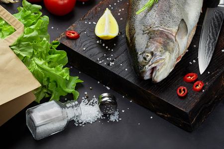 Fish with ingredients - healthy food, diet or cooking concept. Whole raw fish on dark vintage texture. Food background, top view, flat lay style.の写真素材