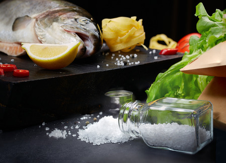 Fish with ingredients - healthy food, diet or cooking concept. Whole raw fish on dark vintage texture. Food background, top view, flat lay style.の写真素材